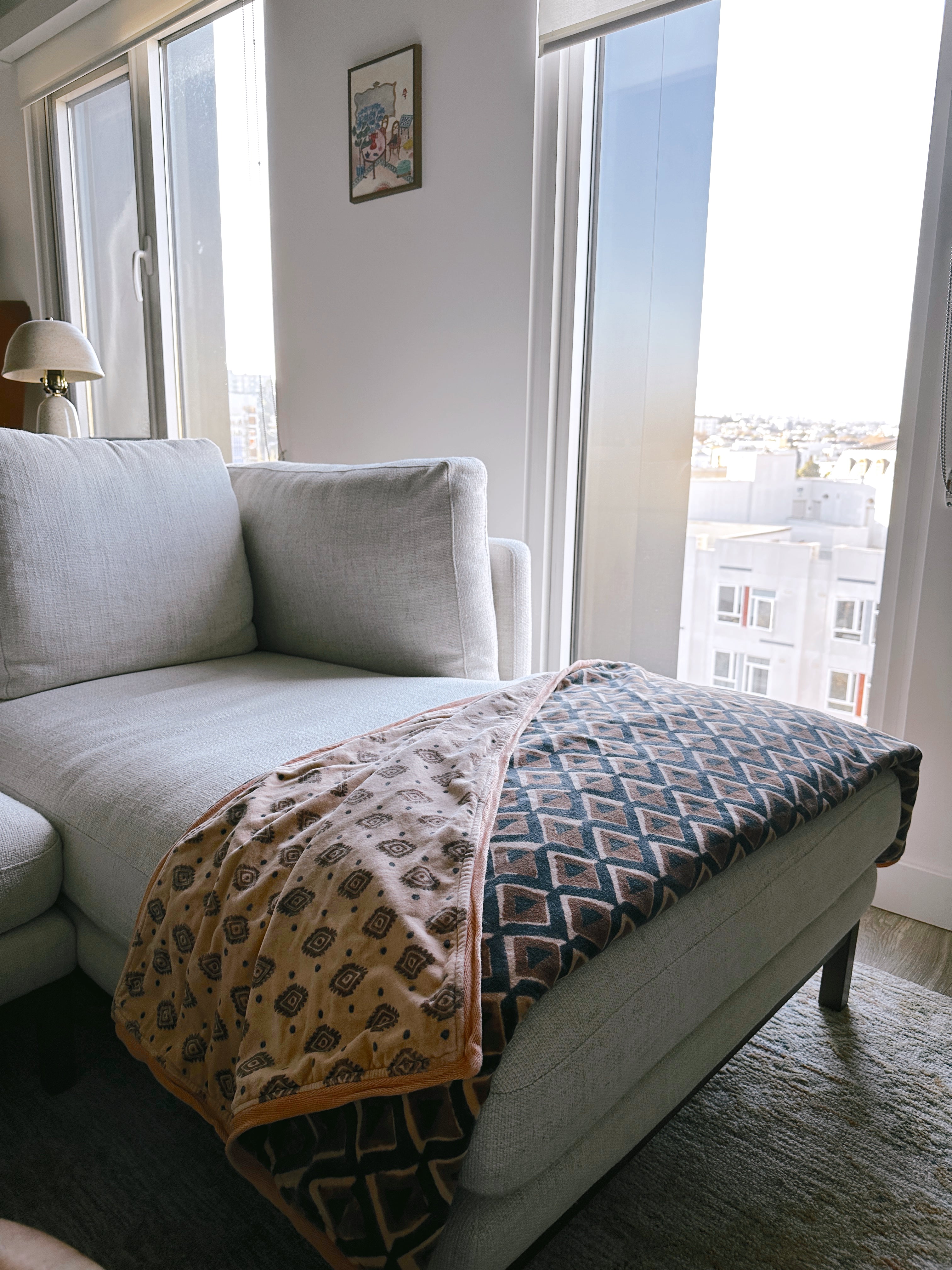 Block print velvet blanket. Tan background with brown diamond print. Reversible print has blue and gold diamond shapes. Displayed on a couch.