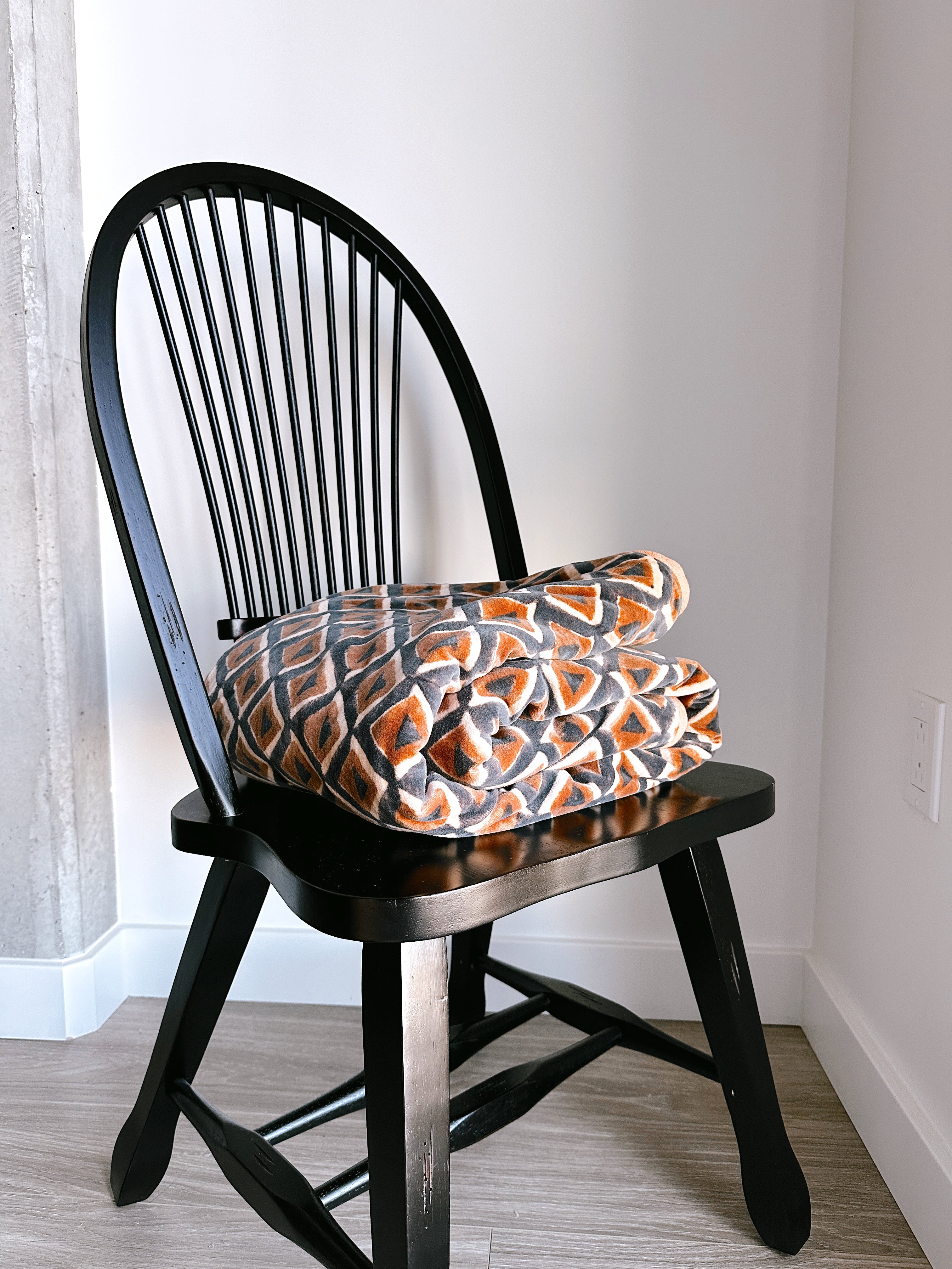 Block print velvet blanket. Tan background with blue and gold diamond shapes, folded on a black chair.