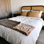 Block print velvet blanket. Tan background with brown diamond print. Reversible print has blue and gold diamond shapes. Displayed at the end of a bed.