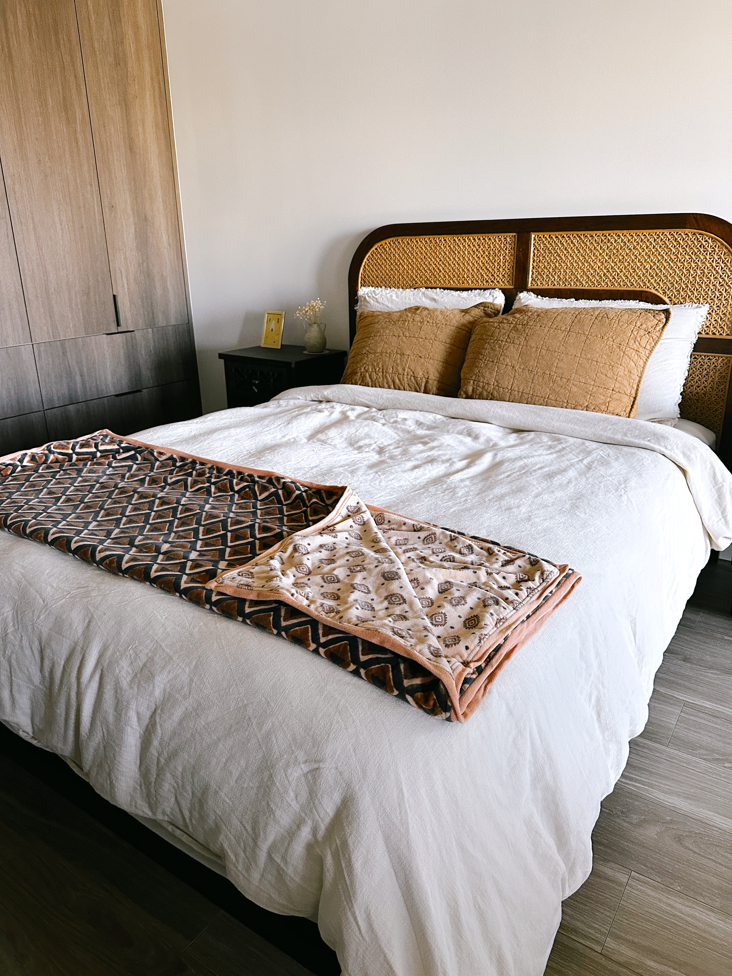 Block print velvet blanket. Tan background with brown diamond print. Reversible print has blue and gold diamond shapes. Displayed at the end of a bed.