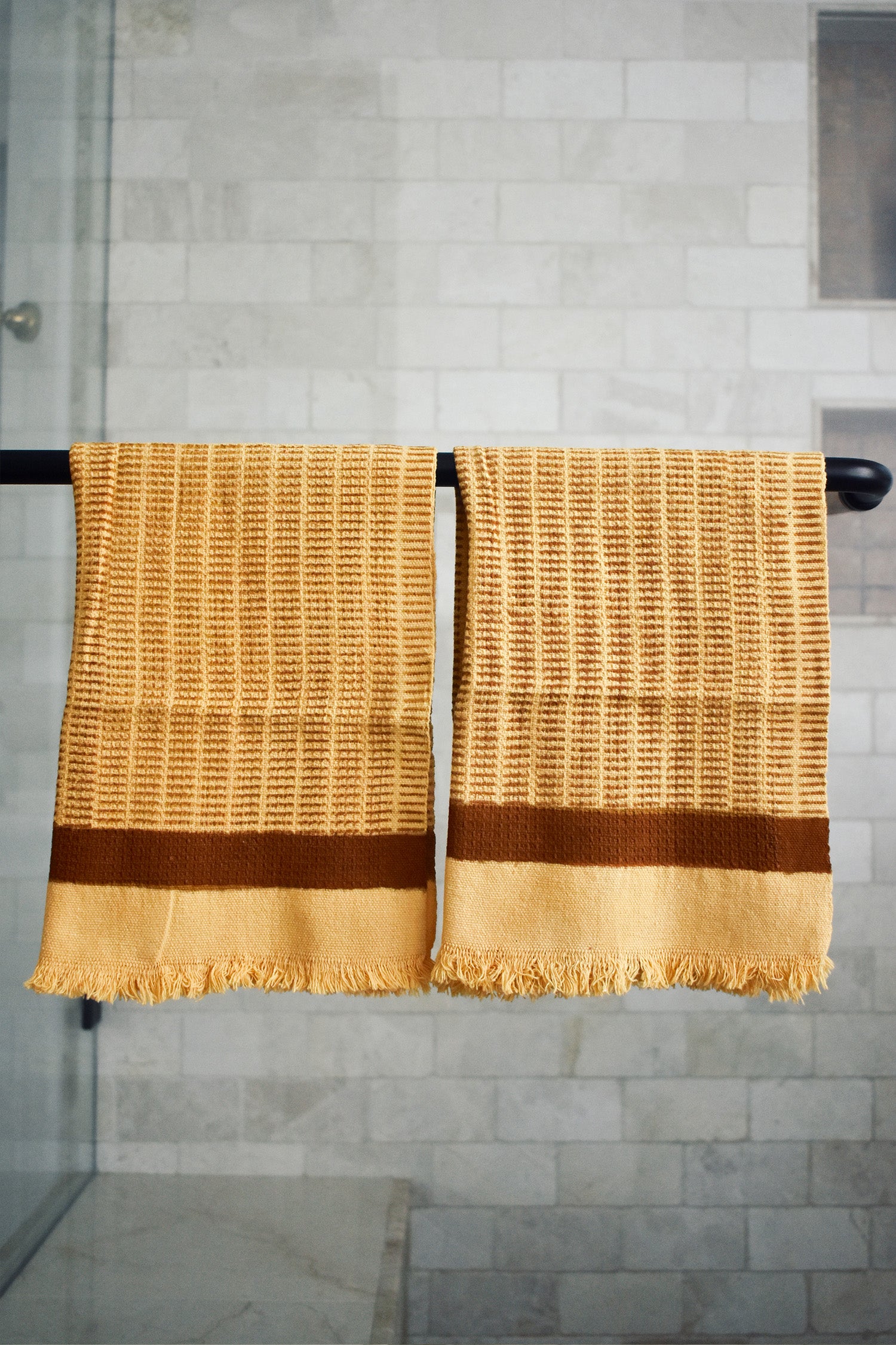 Block printed Feliz hand towels hanging on a black rod outside a shower