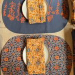 Two Marigold placemats set on a table, one showing the front print and the other showing the back print. Each styled with a plate and folded Marigold napkin on top of the plate