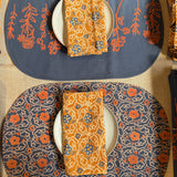 Two Marigold placemats set on a table, one showing the front print and the other showing the back print. Each styled with a plate and folded Marigold napkin on top of the plate