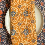 Block printed Marigold orange and blue floral table napkin styled on top of a plate with Marigold placemat