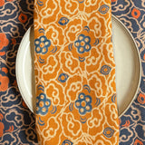 Block printed Marigold orange and blue floral table napkin styled on top of a plate with Marigold placemat