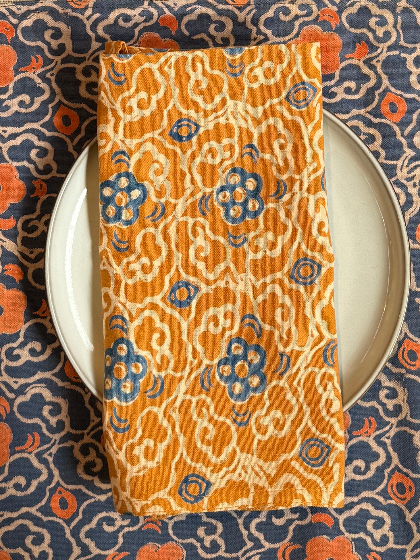 Block printed Marigold orange and blue floral table napkin styled on top of a plate with Marigold placemat