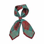 Block printed Monstera bandana, tied up. Bandana has a red leaf print.