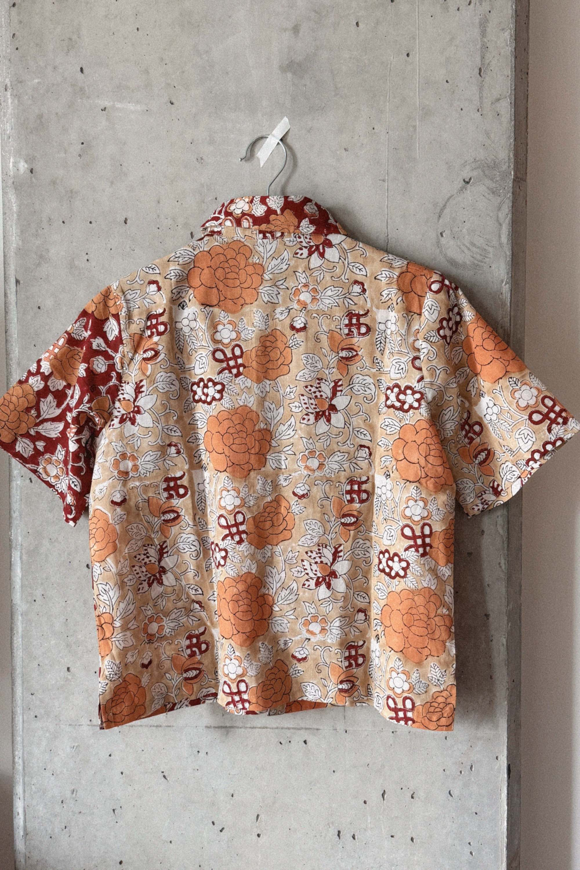 Short-sleeve shirt with a floral pattern hanging on a concrete wall.