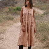 Model wearing sleeveless, cropped jumpsuit outside with heeled brown boots. Jumpsuit has rust floral print, two front pockets and front zipper.