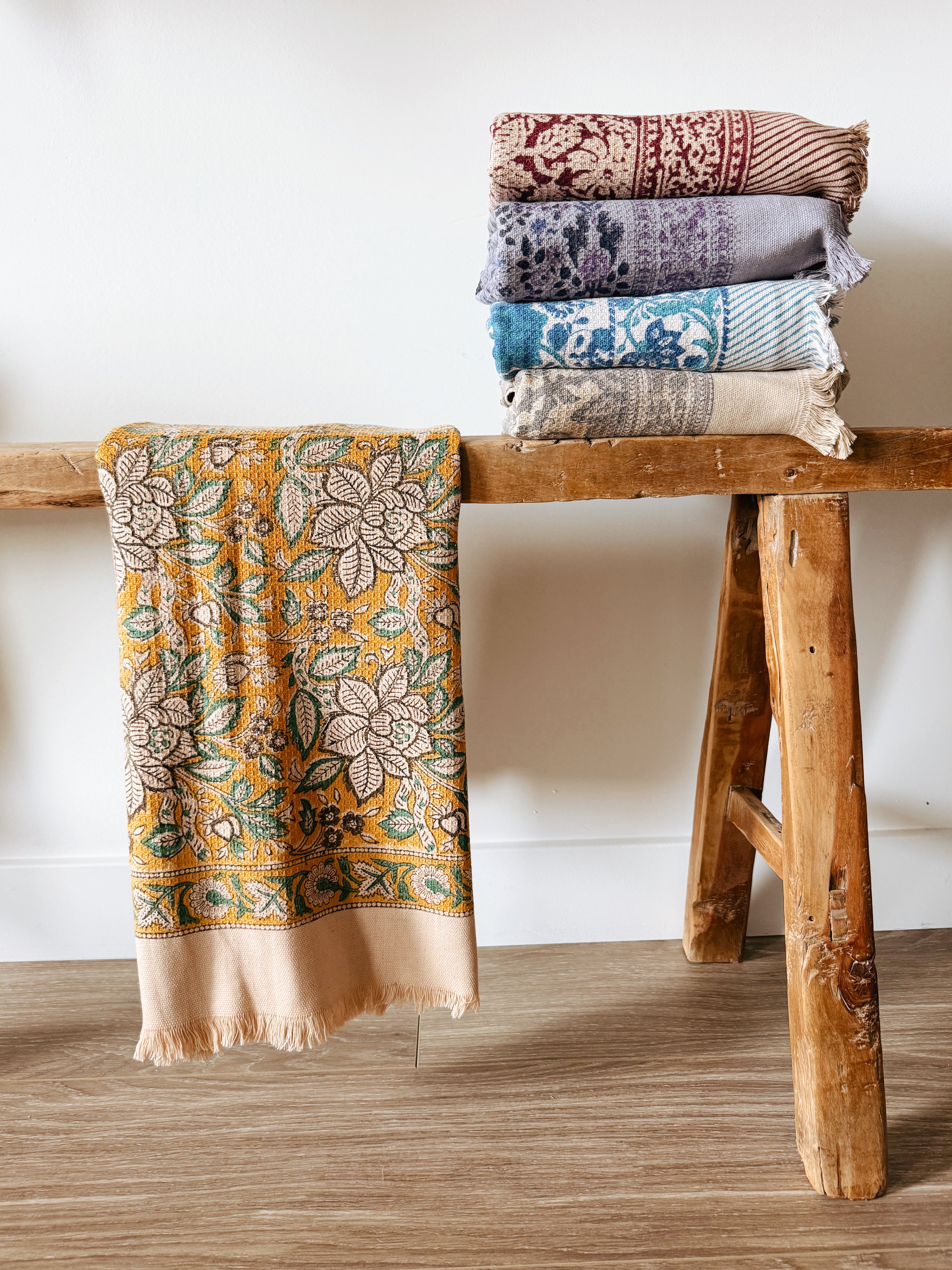 Stack of patterned bath towels on a wooden stool against a white wall
