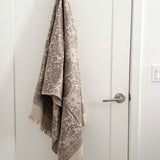 Towel with a grayish floral pattern draped over a door handle on a white door.