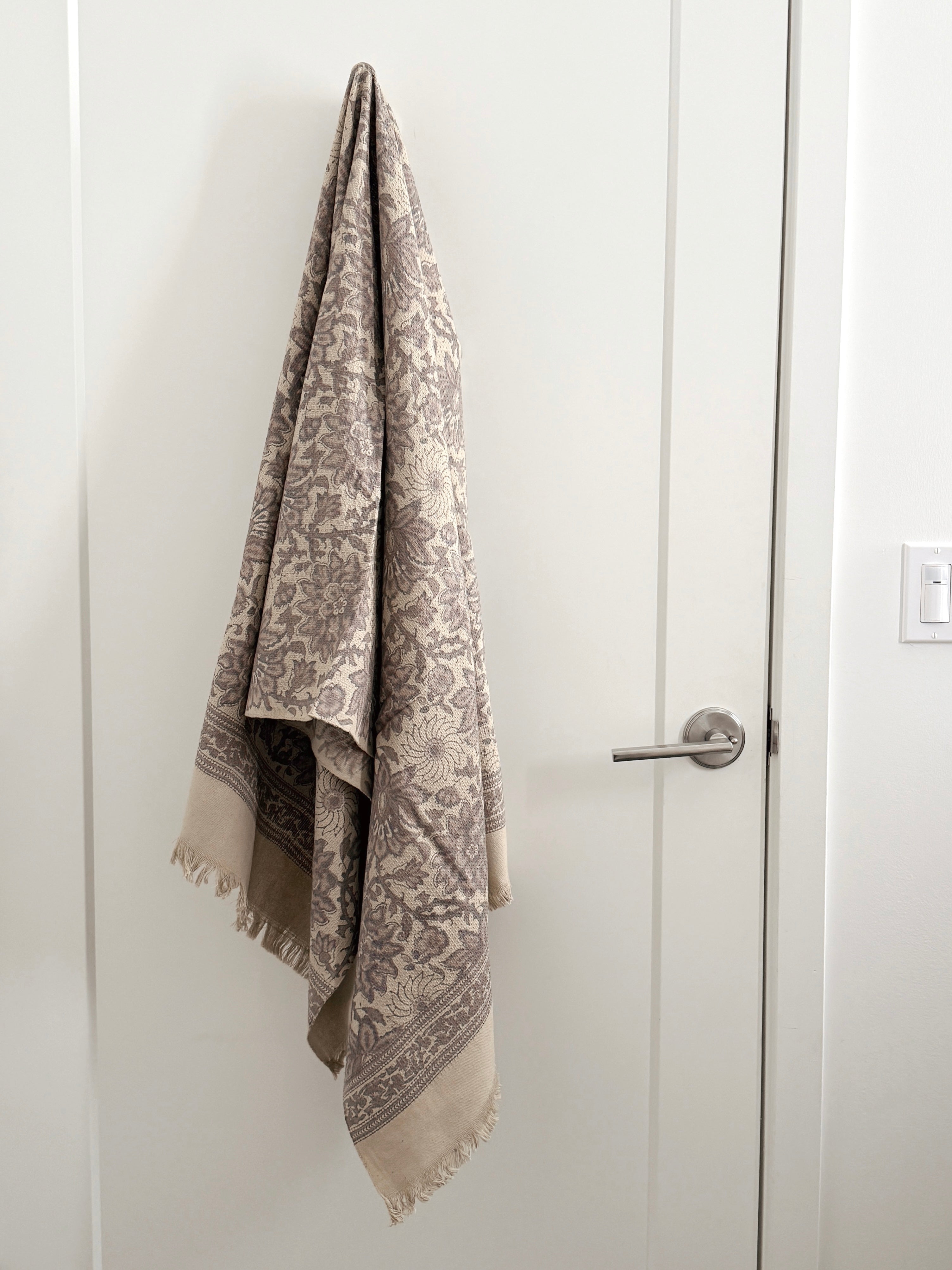 Towel with a grayish floral pattern draped over a door handle on a white door.