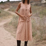 Model wearing sleeveless, cropped jumpsuit outside with heeled brown boots. Jumpsuit has rust floral print, two front pockets and front zipper.