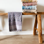 Stack of patterned towels on a wooden stool against a white wall.