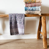 Stack of patterned towels on a wooden stool against a white wall.