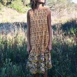 Woman wearing Sharon dress, standing in a field of tall grass. Woman looking up towards the sun.