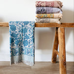 Stack of floral block patterned towels on a wooden stool against a white wall