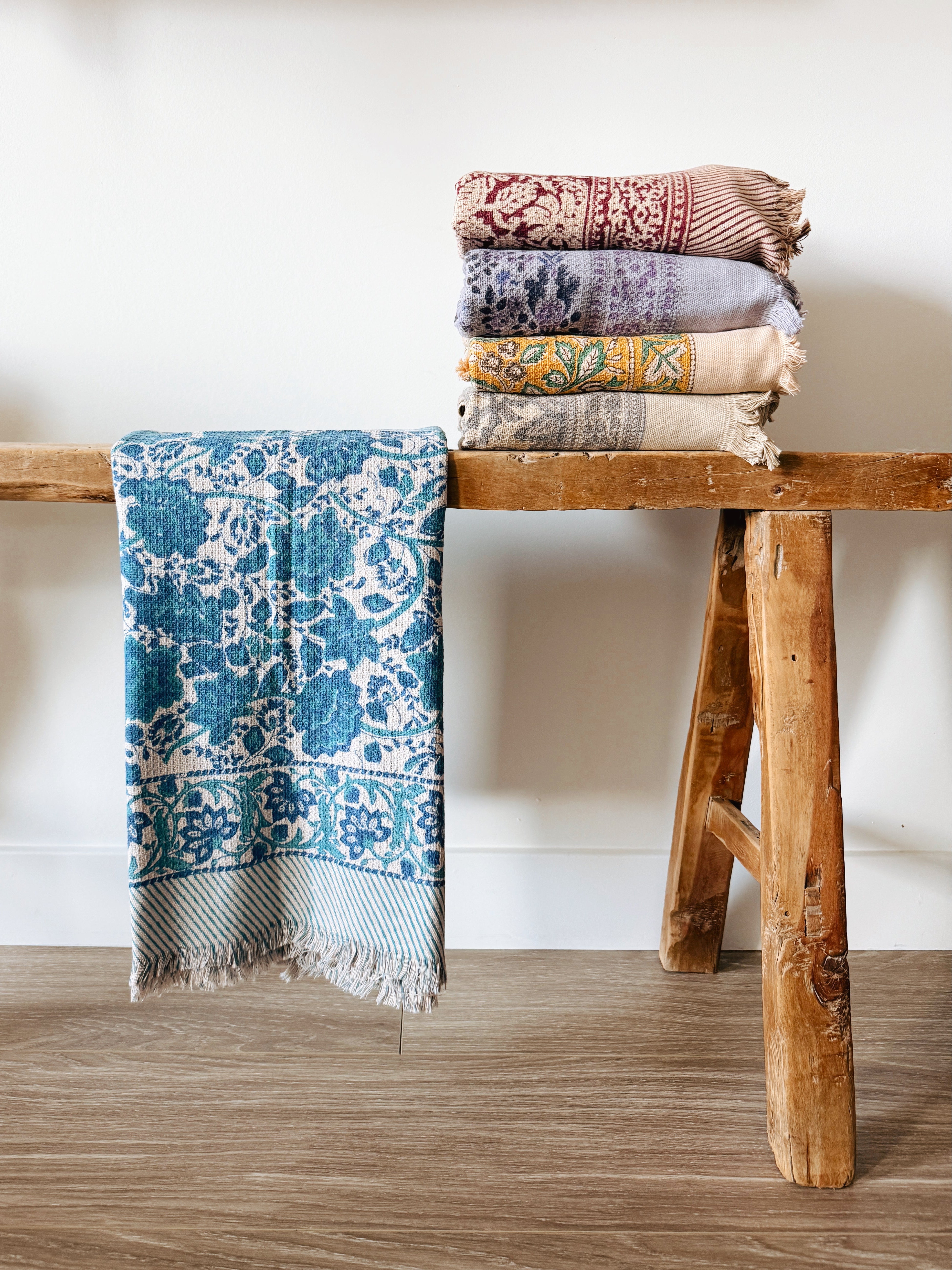 Stack of floral block patterned towels on a wooden stool against a white wall