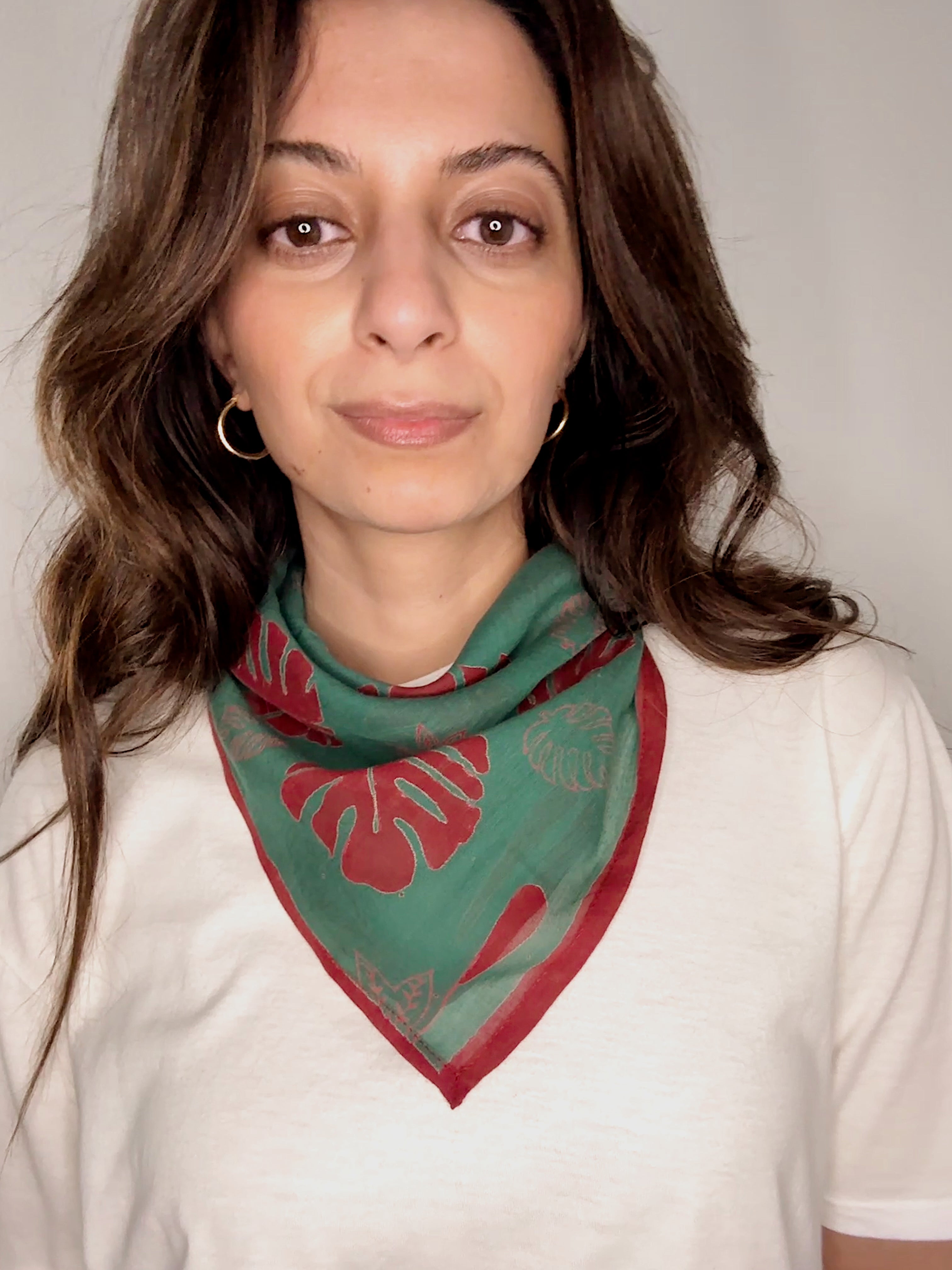 Woman wearing block printed red and green Monstera bandana around the neck
