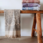 Stack of patterned towels on a wooden bench against a white wall.