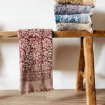 Stack of floral printed bath towels on a wooden stool against a white wall