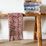 Stack of floral printed bath towels on a wooden stool against a white wall