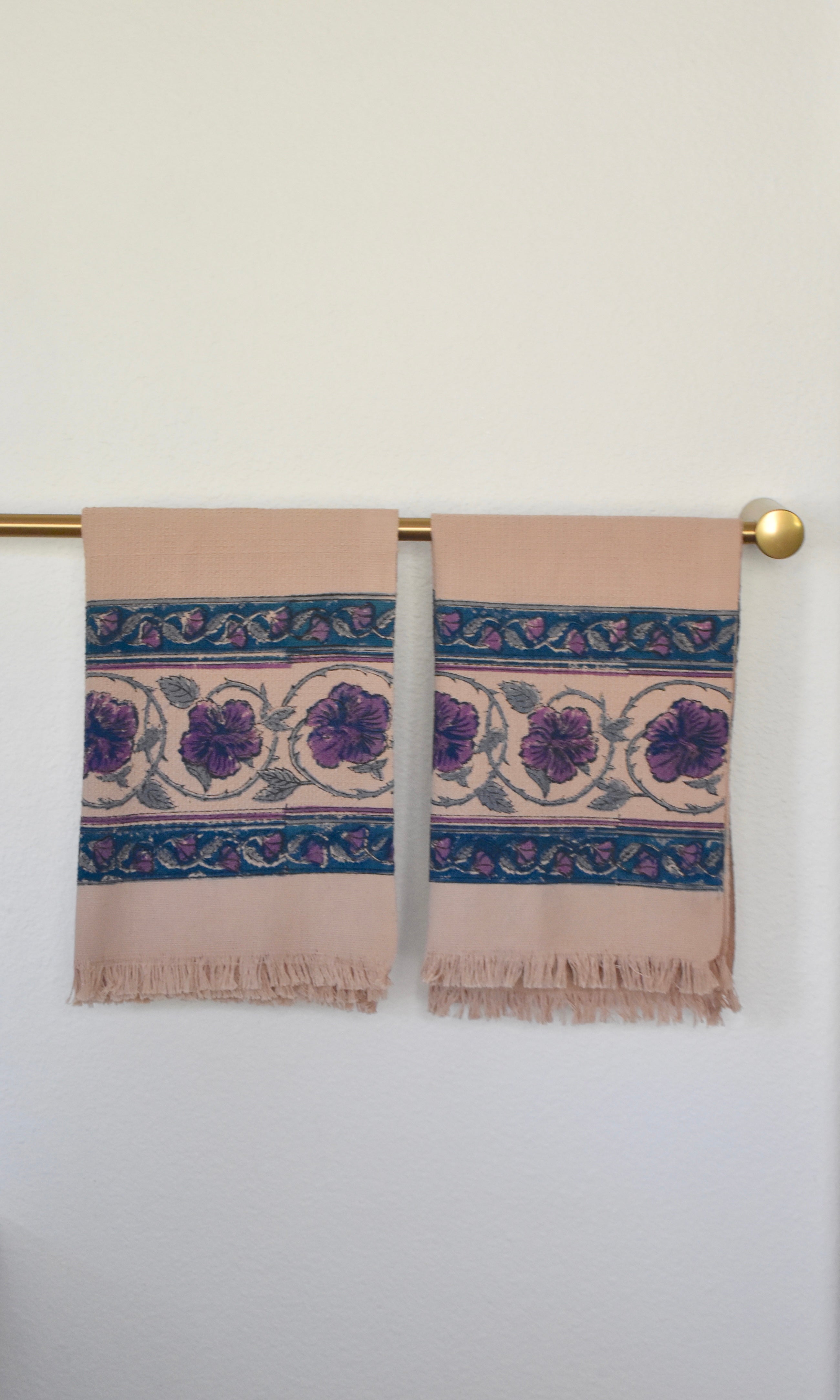 Block printed Lilac Khadi hand towels hanging on a golden rod. Towels have a large floral border print.
