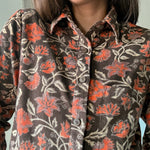 Close up of block printed, brown corduroy shirt with orange and beige flowers. Shirt has one breast pocket.