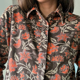 Close up of block printed, brown corduroy shirt with orange and beige flowers. Shirt has one breast pocket.