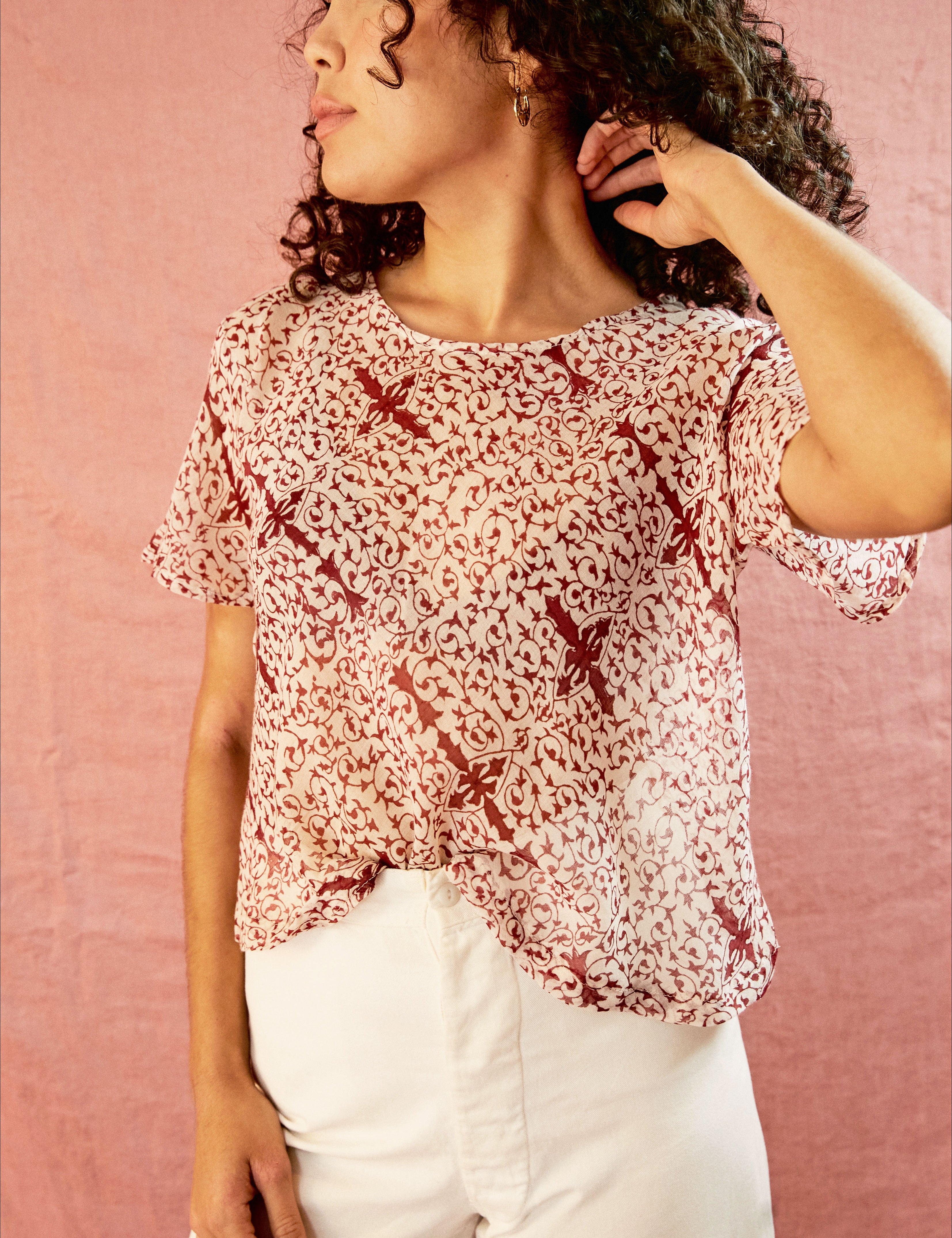 Model wearing the Alicia Top with white pants, against a pink backdrop.
