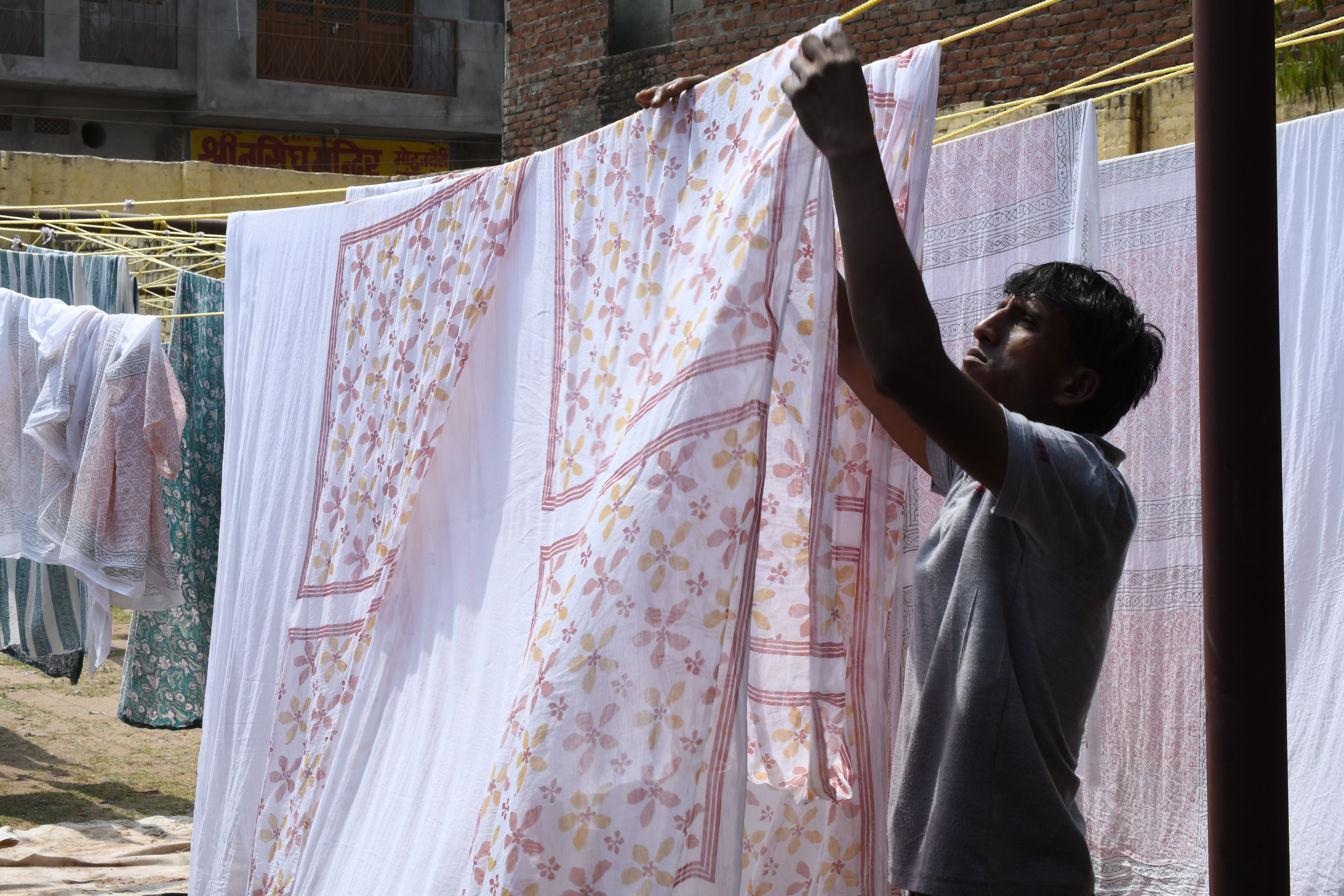 Man hanging up block printed fabric on a clothing line outside