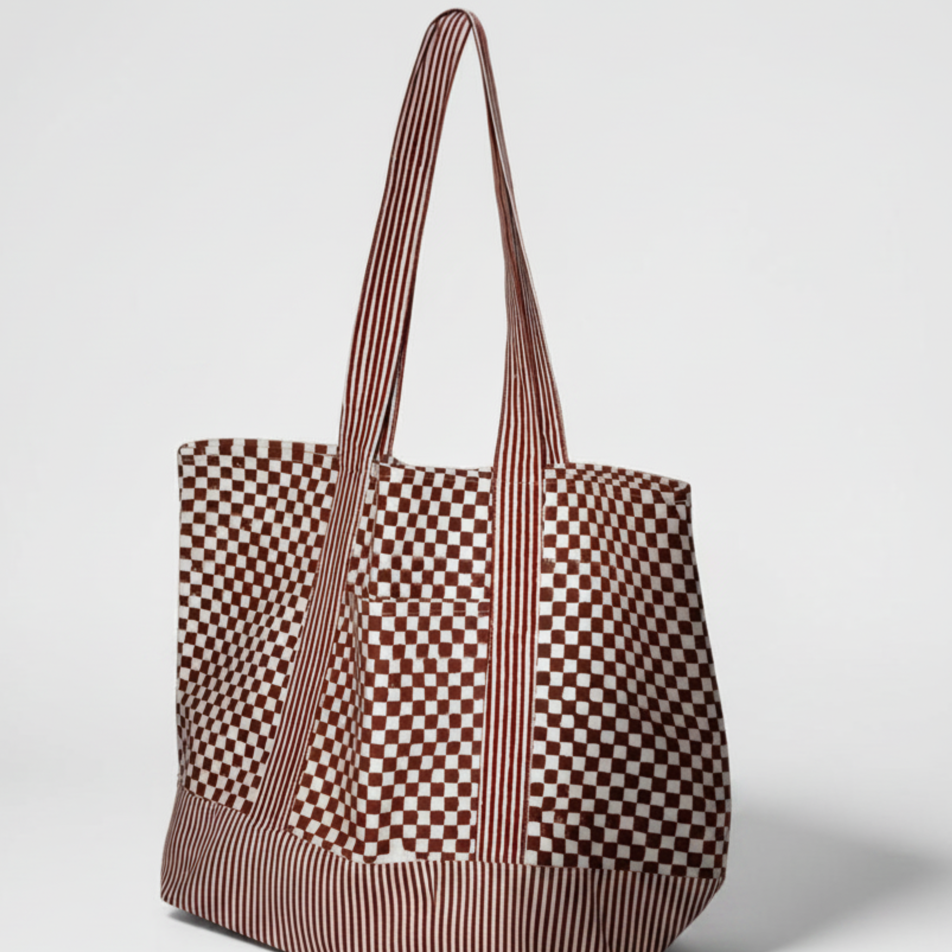 Block print striped and checkered tote bag in red and white standing up against a light grey background