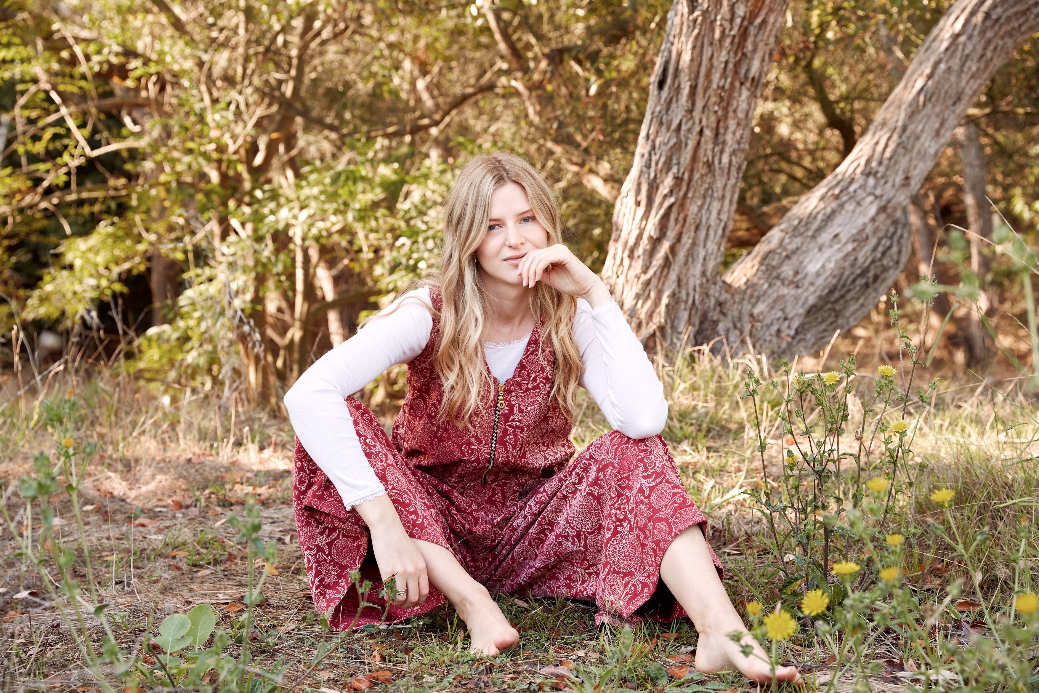 Model wearing the Estella Corduroy Jumpsuit, sitting down in a park with a white long sleeve underneath