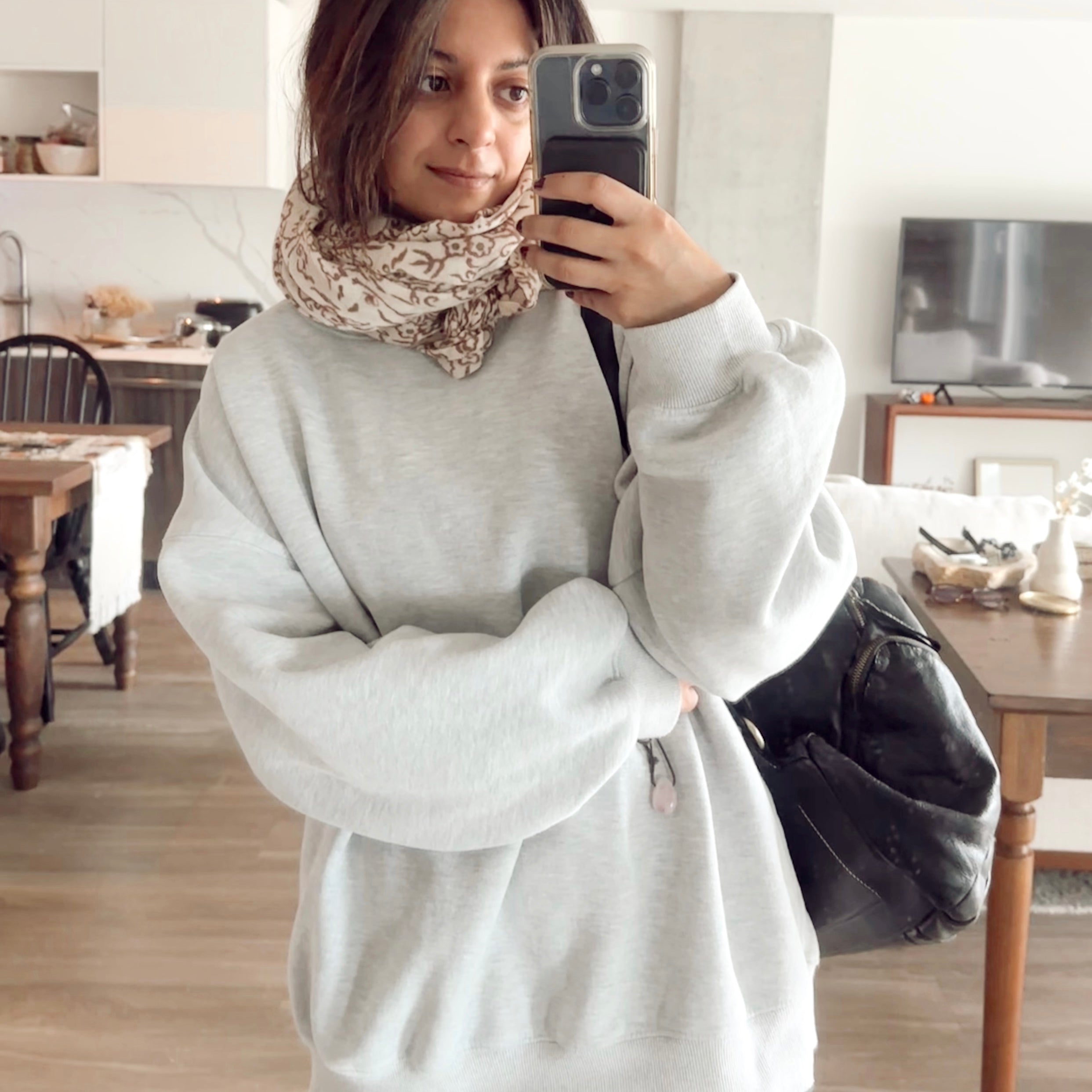 Woman wearing block printed floral printed wool scarf, bundled around neck paired with a grey sweatshirt, taking a selfie