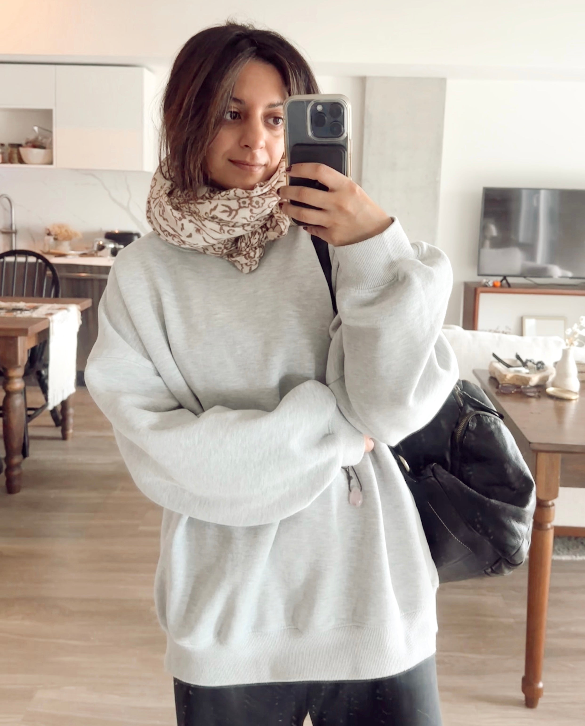 Woman wearing block printed floral printed wool scarf, bundled around neck paired with a grey sweatshirt, taking a selfie