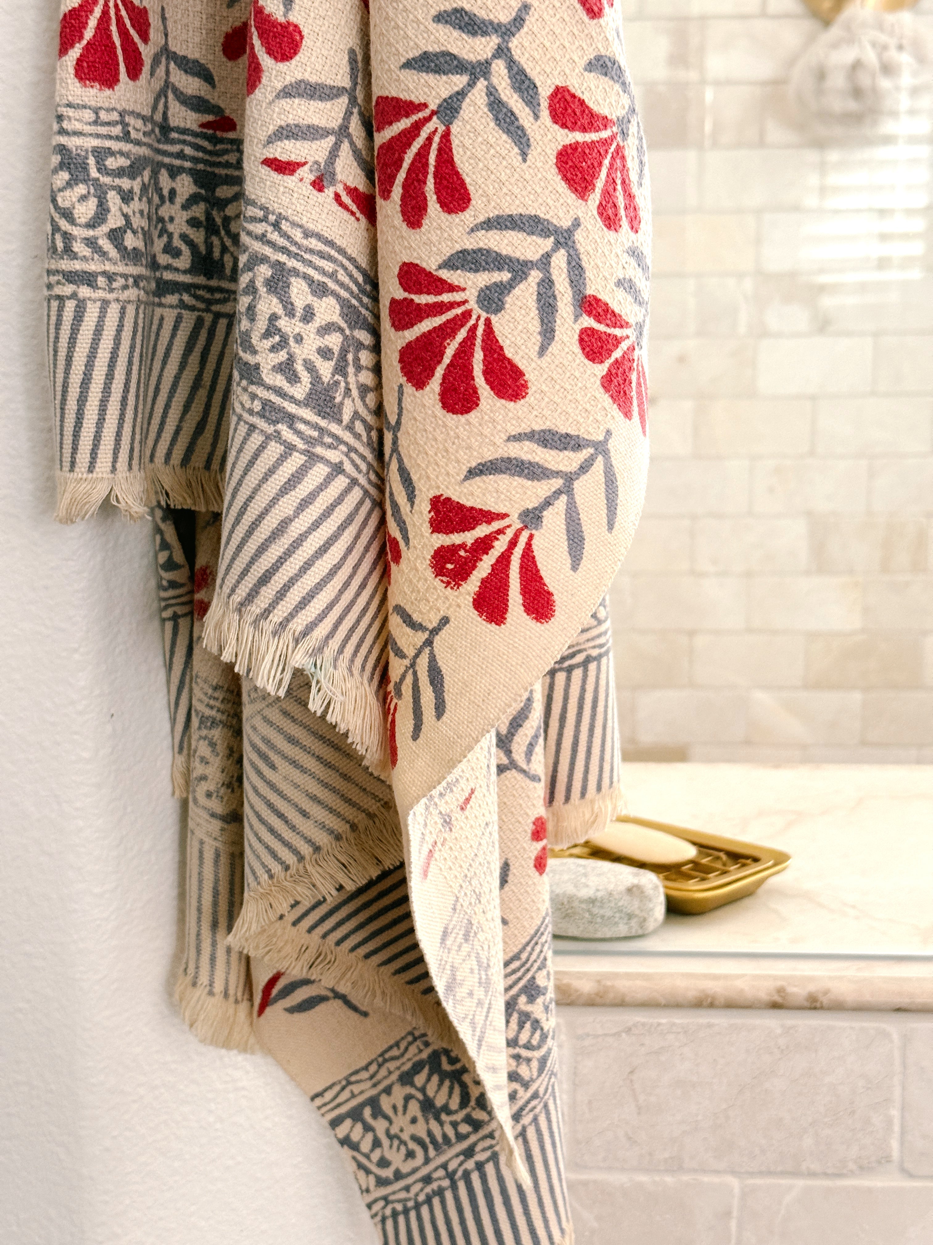 A beige woven towel with red and gray botanical and geometric patterns hung in front of a tiled shower
