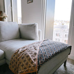 Block print velvet blanket. Tan background with brown diamond print. Reversible print has blue and gold diamond shapes. Displayed on a couch. 