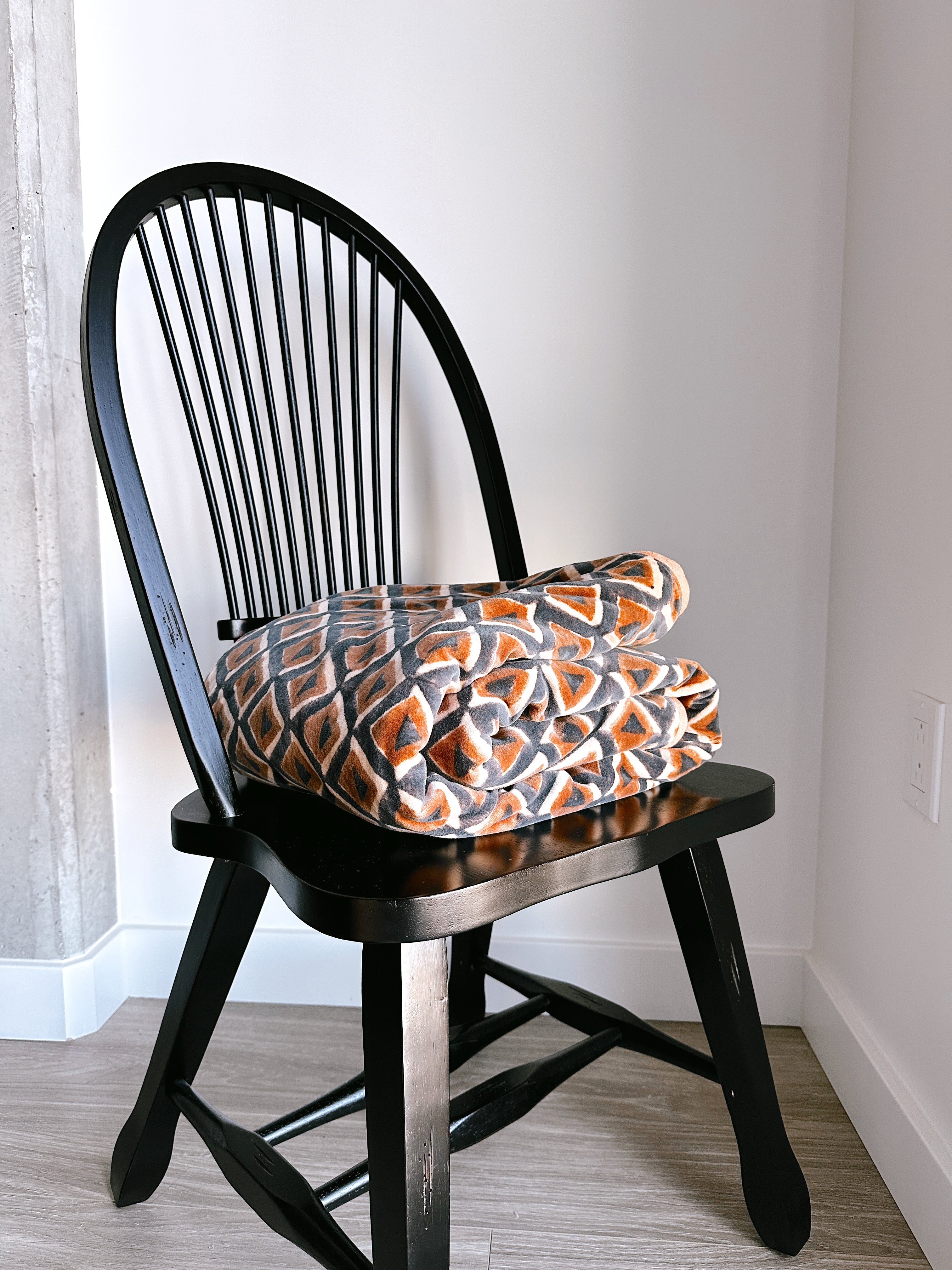 Block print velvet blanket. Tan background with blue and gold diamond shapes, folded on a black chair. 