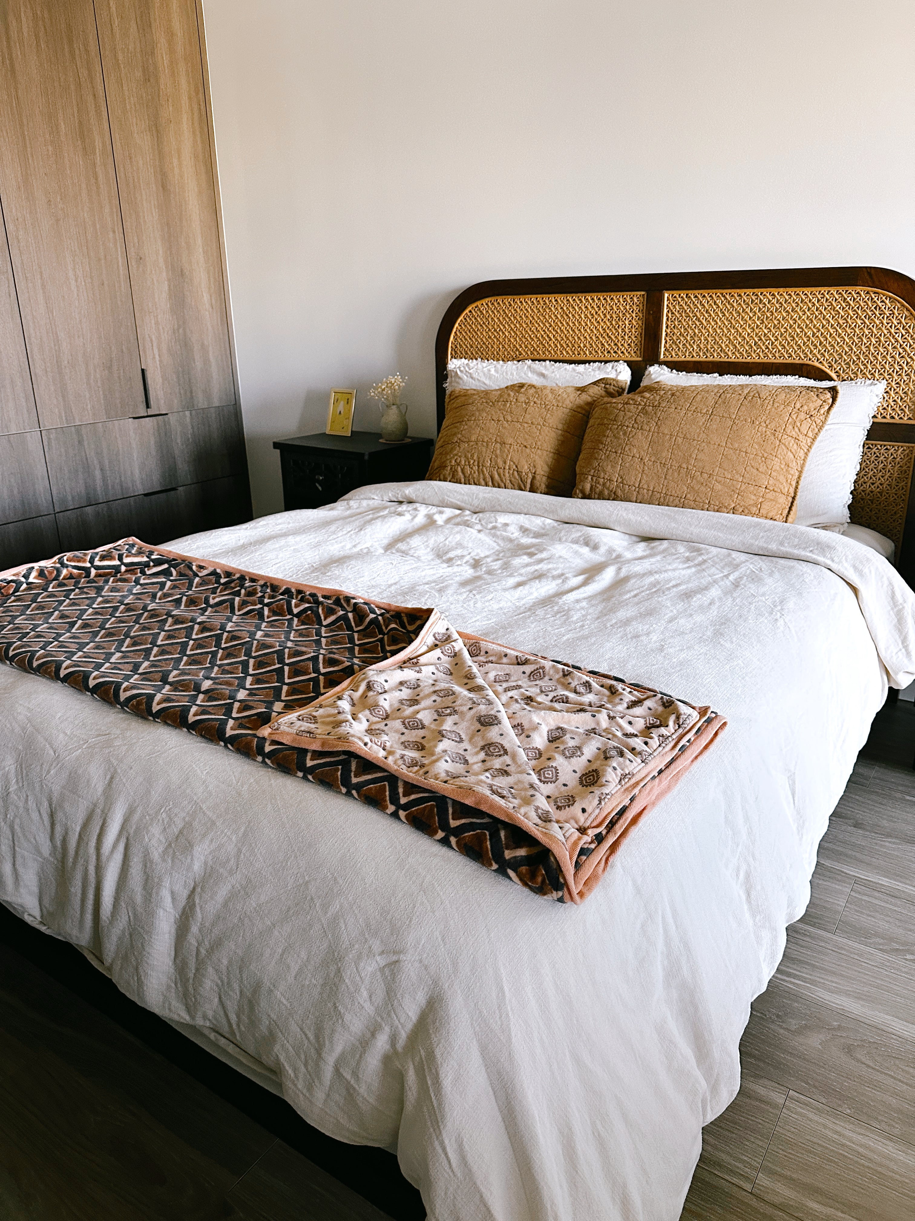 Block print velvet blanket. Tan background with brown diamond print. Reversible print has blue and gold diamond shapes. Displayed at the end of a bed. 