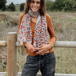 Woman wearing block printed Alia georgette scarf around the neck, paired with orange long sleeve and black jeans. Woman is standing outside in front of a fence.