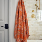 Block printed orange floral printed khadi bath towel hanging on a golden hook