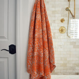 Block printed orange floral printed khadi bath towel hanging on a golden hook