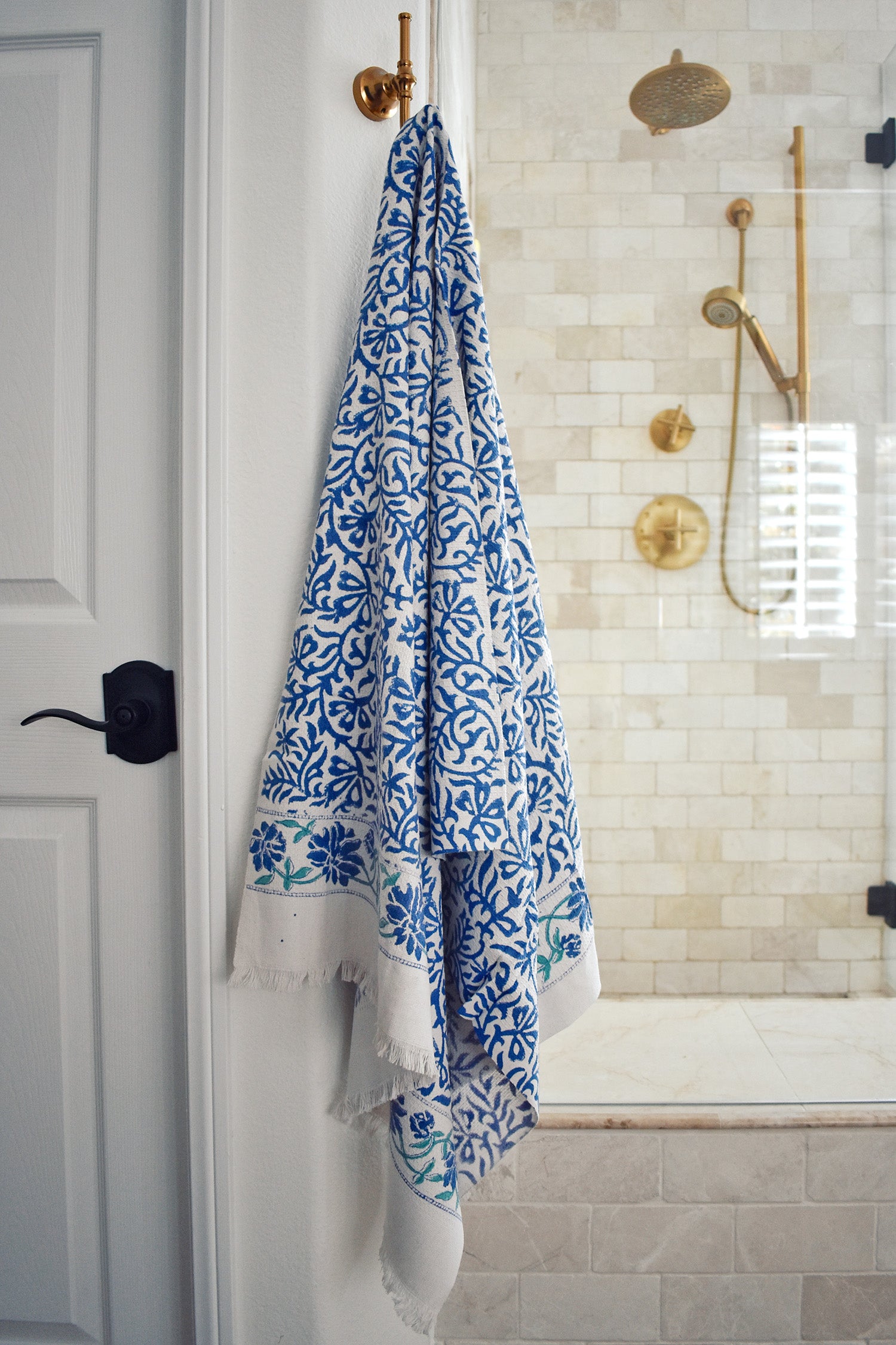 Block printed Athena bath towel hanging on a hook in front of a shower