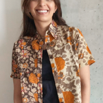 Woman wearing a grey and orange floral patterned shirt over a blakc dress against a concrete wall.