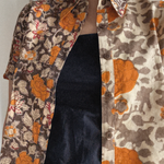 Person wearing a floral patterned shirt with orange, grey and brown colors. Shirt is worn over a black dress. 