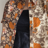Person wearing a floral patterned shirt with orange, grey and brown colors. Shirt is worn over a black dress. 