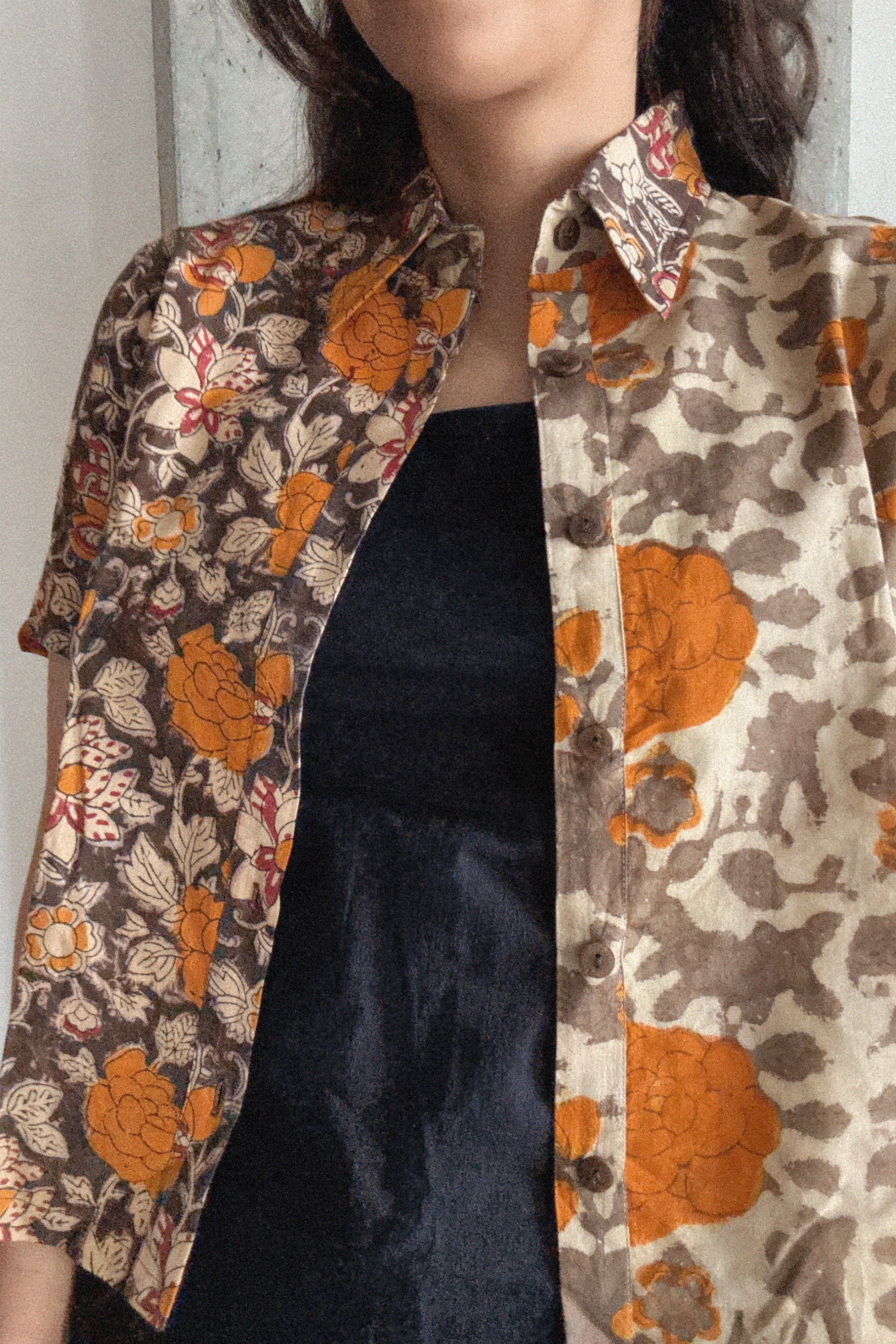 Person wearing a floral patterned shirt with orange, grey and brown colors. Shirt is worn over a black dress. 
