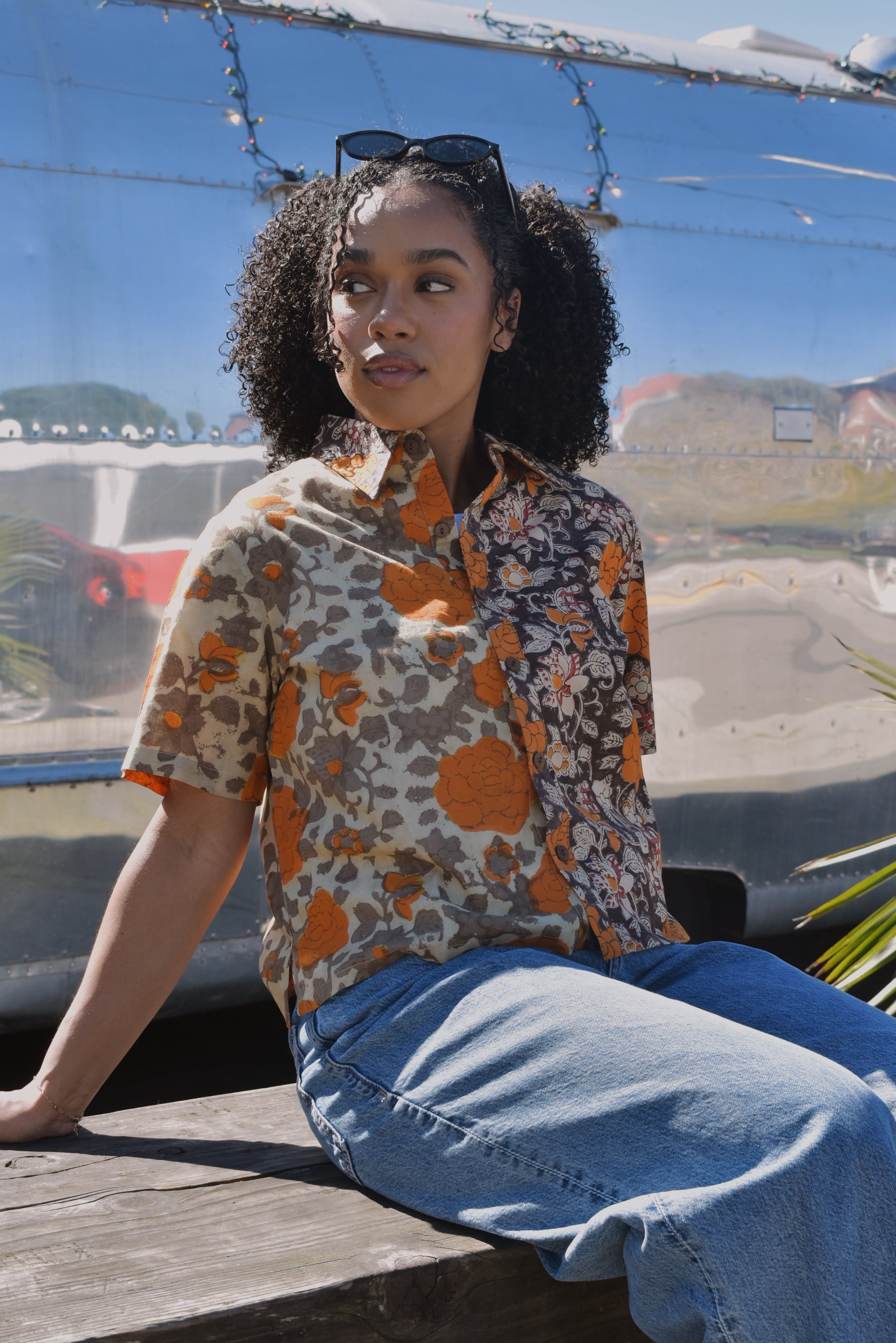 Woman in a floral shirt and jeans sitting outdoors in front of an RV