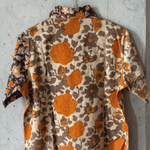 Orange and grey floral patterned shirt on a hanger against a concrete wall, showing the back