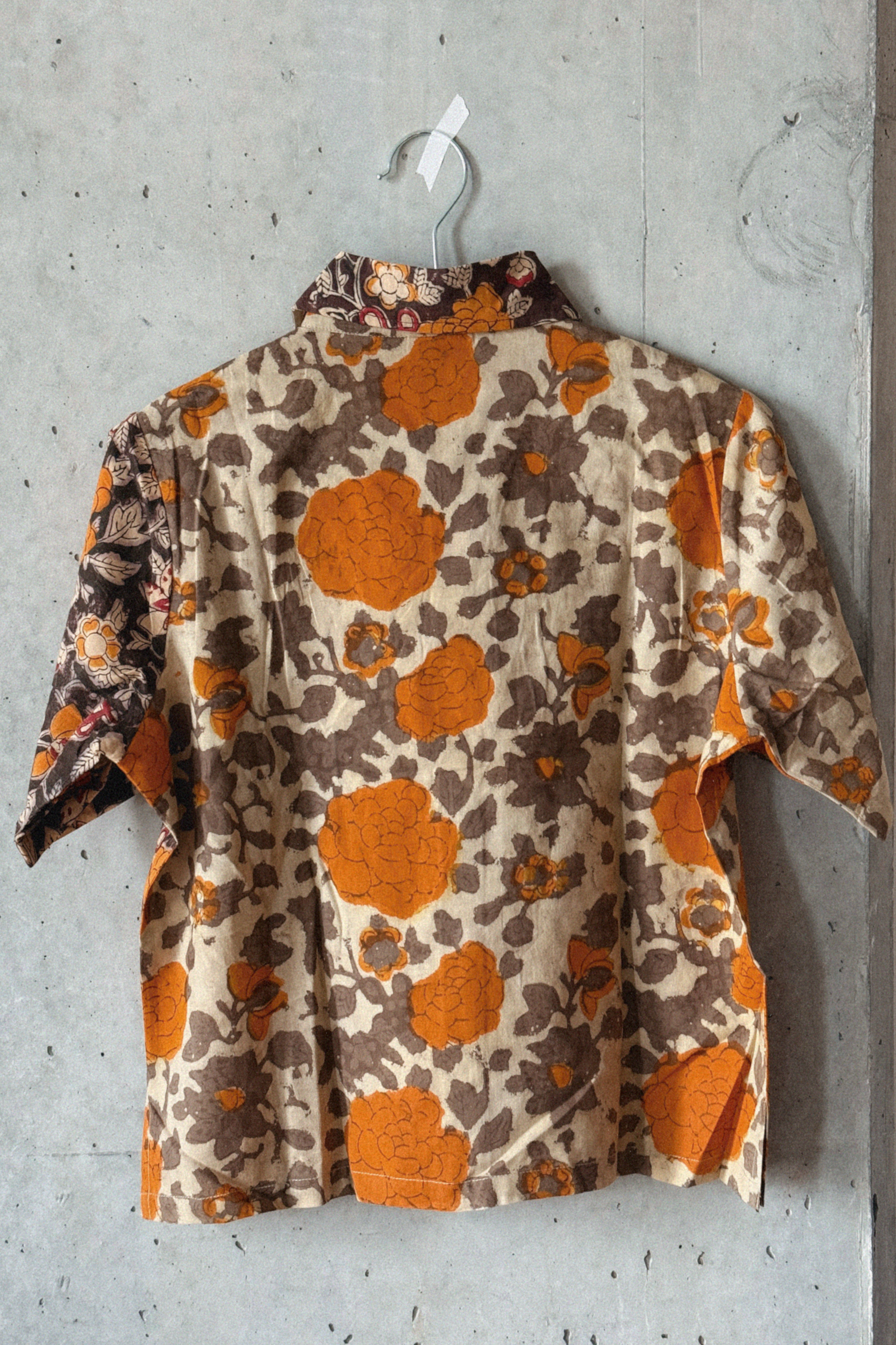 Orange and grey floral patterned shirt on a hanger against a concrete wall, showing the back